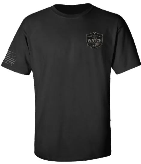 A black short-sleeve crewneck t-shirt with a dark gray 'The Watch' shield logo on the left chest and a distressed American flag graphic with 'RESIST' on the right sleeve, shown on a plain white background.